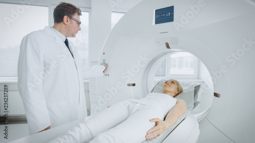 In Medical Laboratory Radiologist Controls MRI or CT or PET Scan with Female Patient Undergoing Procedure. Professional Doctor Conducts Emergency Checkup Procedure with Advanced Medical Technologies.