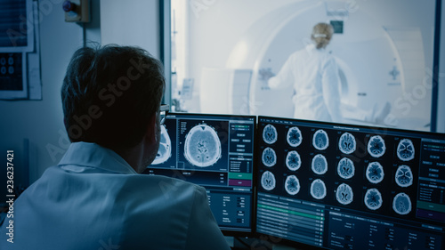 Billede på lærred In Medical Laboratory Patient Undergoes MRI or CT Scan Process under Supervision of Radiologist, in Control Room Doctor Watches Procedure and Monitors with Brain Scans Results