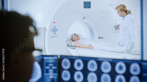 In Medical Laboratory Patient Undergoes MRI or CT Scan Process under Supervision of Radiologist  in Control Room Doctor Watches Procedure and Monitors with Brain Scans Results.