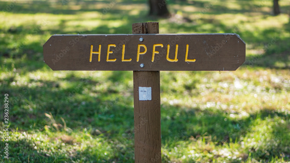 Brown wooden sign in grassy field with helpful written on it