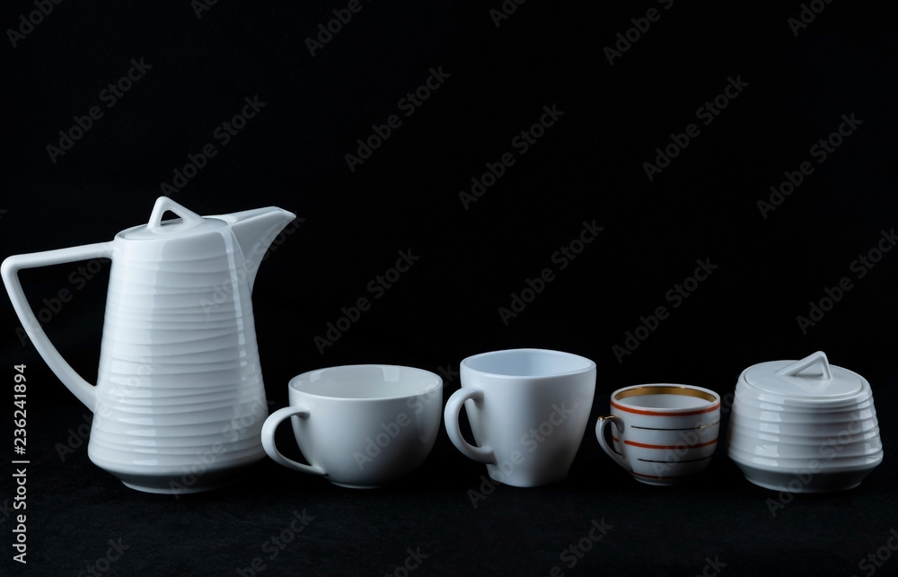 Three cups of different sizes, a teapot for tea and sugar bowl stand on a black background. Three cups of different sizes, a teapot for tea and sugar bowl stand on a black background.