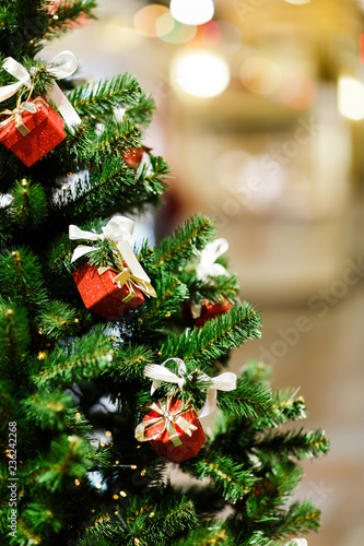 Image of decorated Christmas spruce with red gift boxes in store .