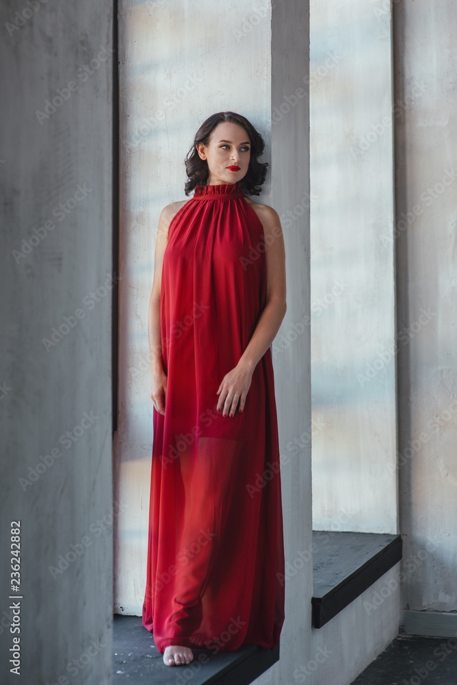 portrait of beautiful young brunette muse woman in red long dress near the window portrait of beautiful young brunette muse woman in red long dress near the window