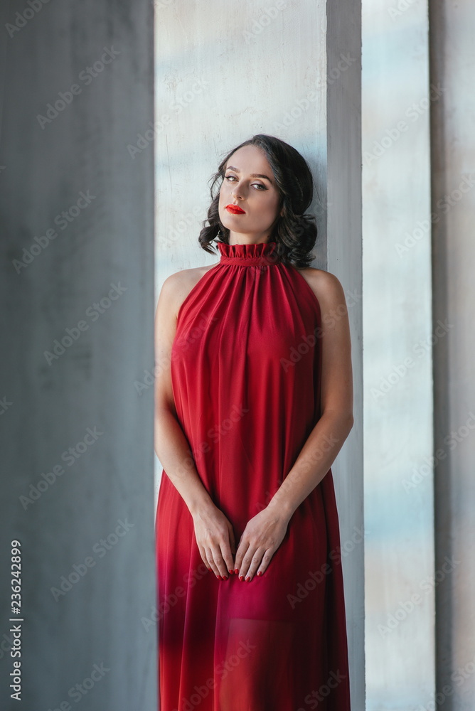 portrait of beautiful young brunette muse woman in red long dress near the window portrait of beautiful young brunette muse woman in red long dress near the window