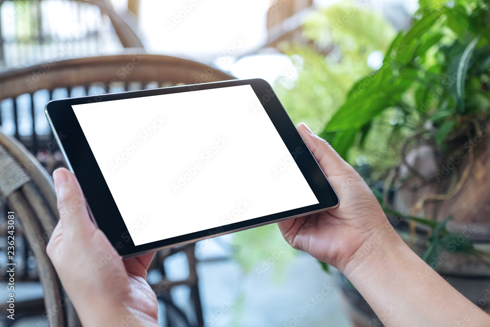 Mockup image of hands holding and using black tablet pc with blank white desktop screen while sitting in the outdoors