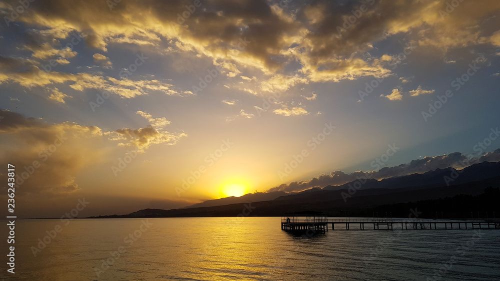 A sunset above lake with pier and mountains with blue sky and clouds