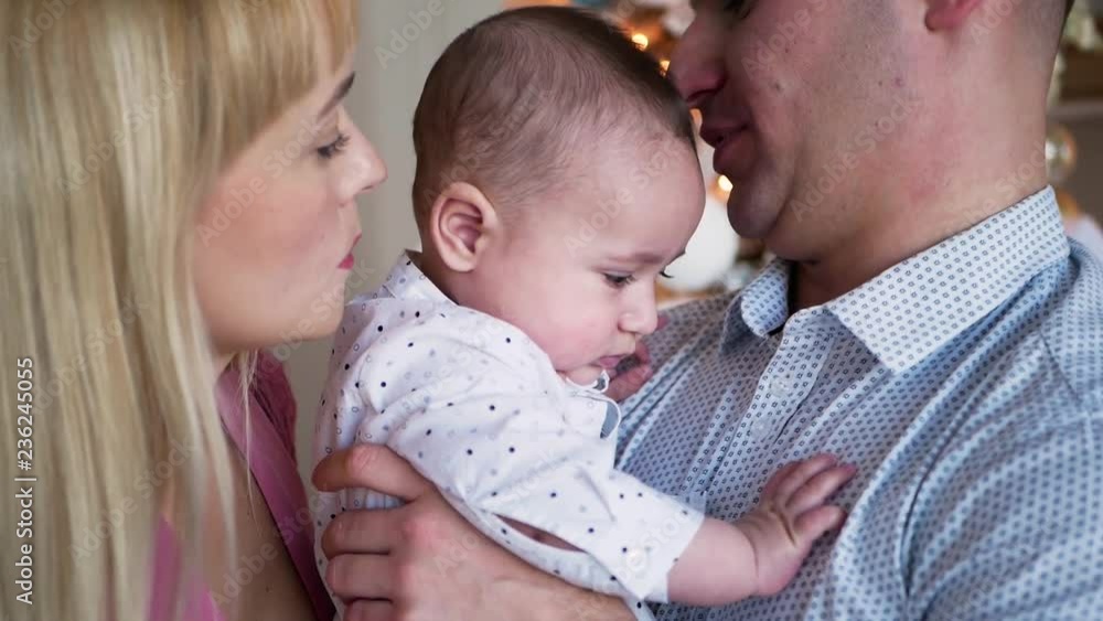 parents hold their son in the hands of standing in the room at the christmas tree parents hold their son in the hands of standing in the room at the christmas tree