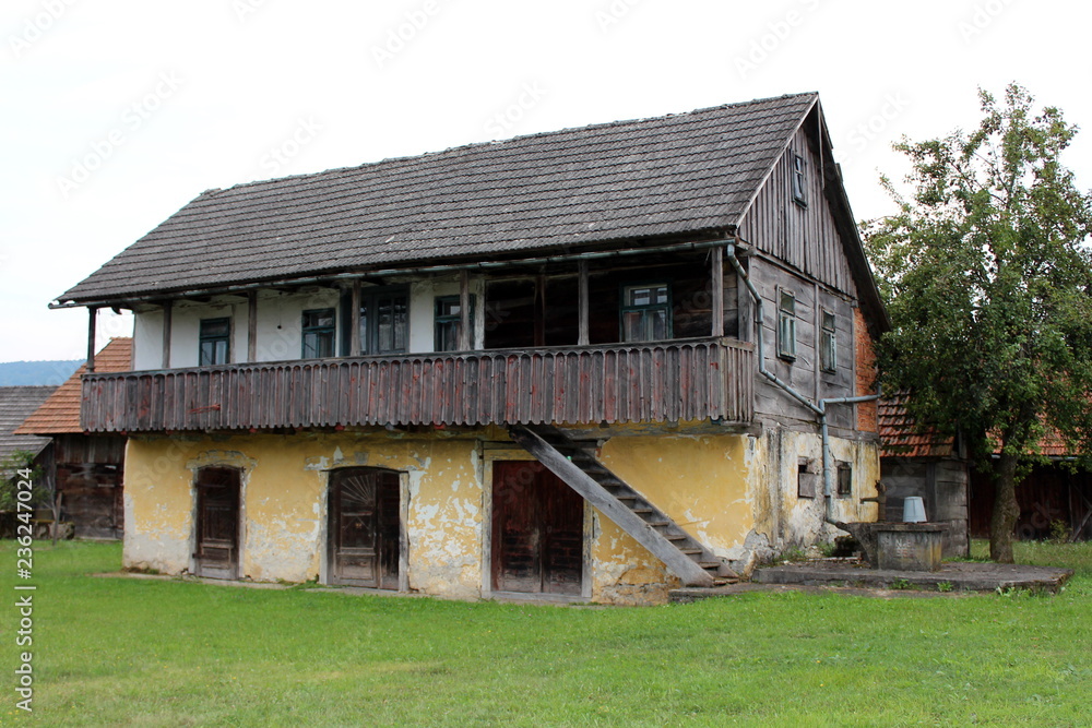 Large old wooden family house with raised front porch overlooking surroundings, dilapidated boards and broken windows next to concrete well with rusted water pump and tall tree on dark gloomy summer d Large old wooden family house with raised front porch overlooking surroundings, dilapidated boards and broken windows next to concrete well with rusted water pump and tall tree on dark gloomy summer d