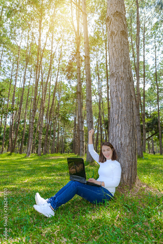 Portrait of pretty young woman sitting on green grass in park summer day while using laptop