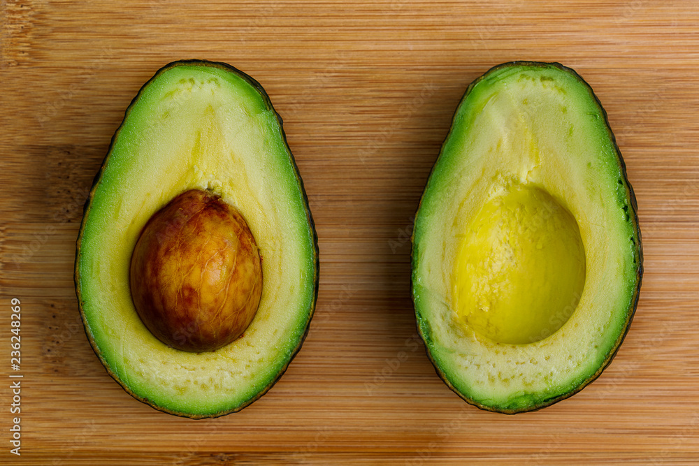 Two halves of an avocado face up with the pit still in place, on a bamboo cutting board.