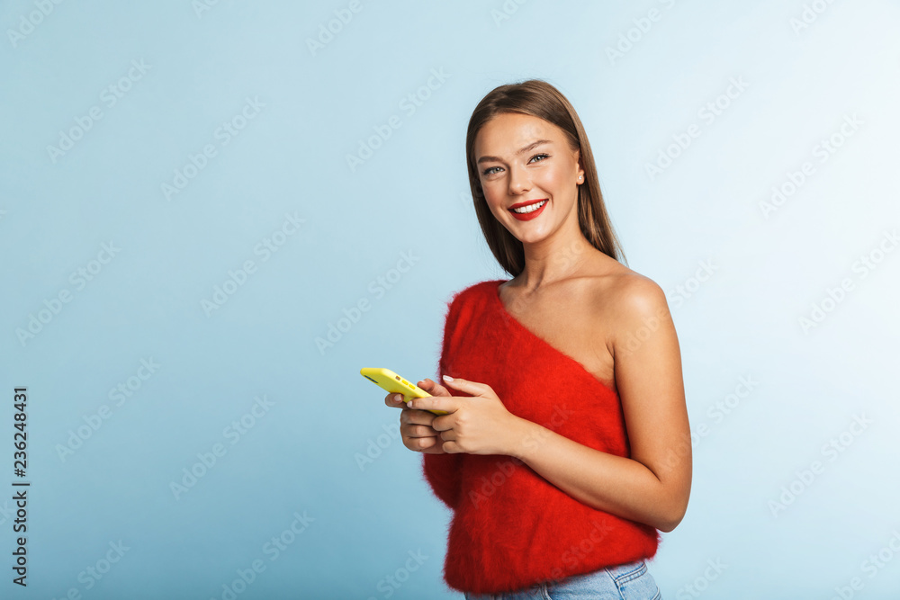 Smiling young woman posing isolated over blue wall background using mobile phone. Smiling young woman posing isolated over blue wall background using mobile phone.