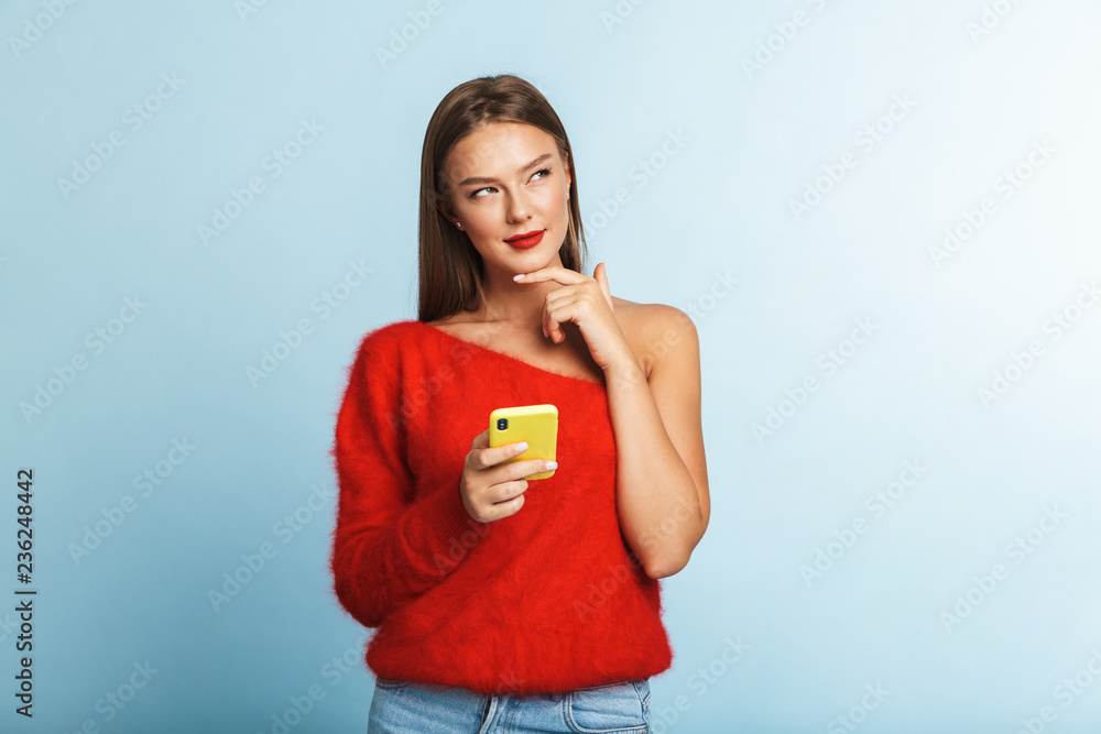 Dreaming thinking young woman posing isolated over blue wall background using mobile phone. Dreaming thinking young woman posing isolated over blue wall background using mobile phone.