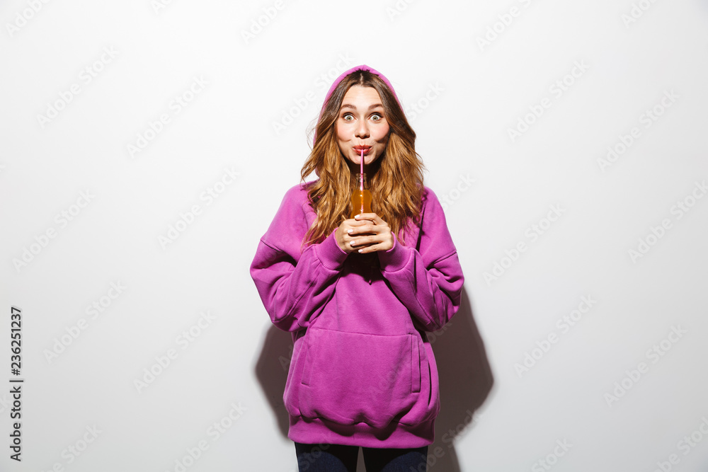 Portrait of cheerful woman 20s wearing sweatshirt drinking soda using straw, isolated over white background Portrait of cheerful woman 20s wearing sweatshirt drinking soda using straw, isolated over white background
