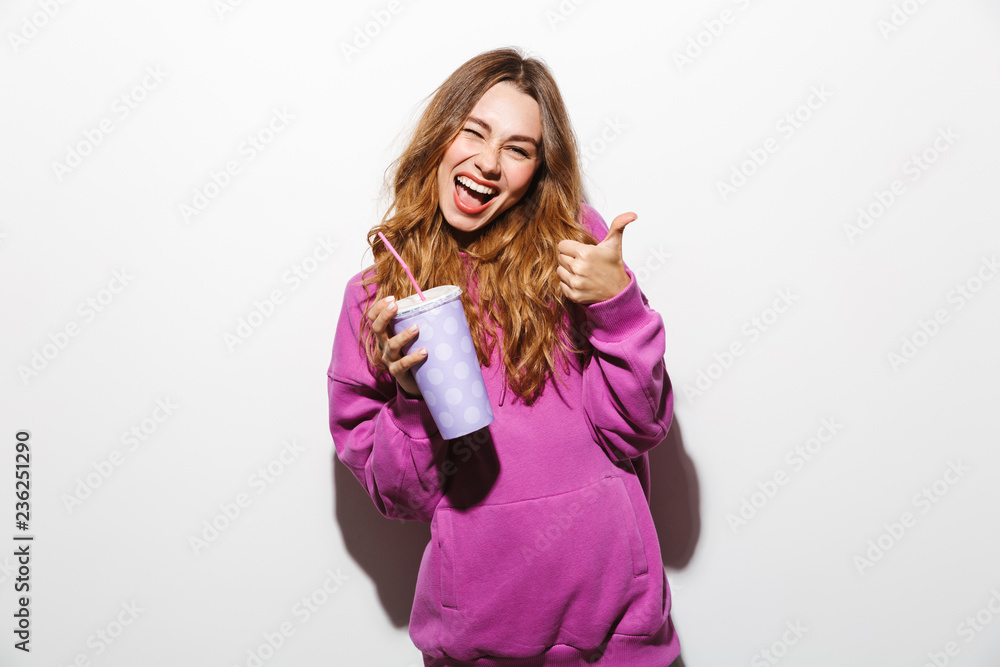Portrait of smiling woman 20s wearing sweatshirt drinking soda from paper cup using straw, isolated over white background Portrait of smiling woman 20s wearing sweatshirt drinking soda from paper cup using straw, isolated over white background