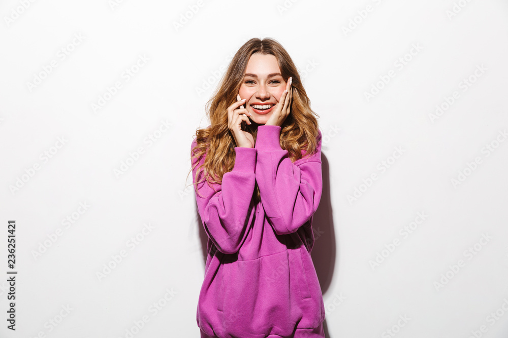 Portrait of adorable woman 20s wearing sweatshirt talking on cell phone while standing, isolated over white background Portrait of adorable woman 20s wearing sweatshirt talking on cell phone while standing, isolated over white background