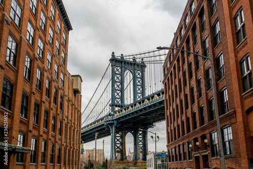 Manhattan Bridge Viewed From Dumbo, Brooklyn, New York between two red brick buildings and cloudy background