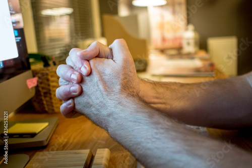 close-up of a man praying with the typical hands gesture in front of the screen of desktop computer in the evening in the home office
