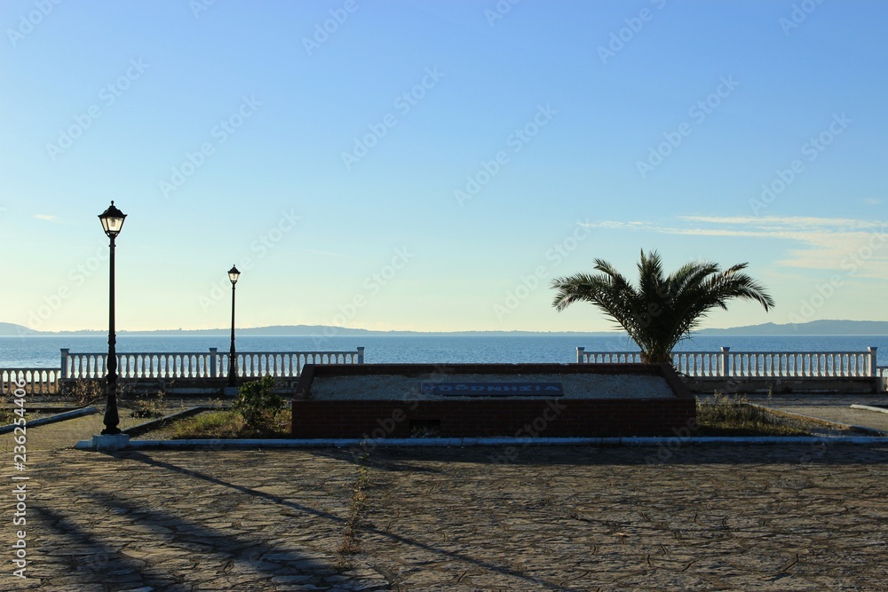 Obraz premium Αmbracian gulf behind the concrete retro fence made of cement from the square of Koronisia village lamps in the foreground square paved with stones on the sign 
