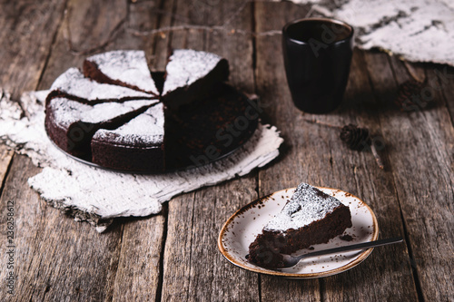 Kladdkaka. Traditional Swedish moist chocolate cake on old rustic wooden table decorated dry twigs, pine cones and birch bark. Fika. Hygge. Toned image