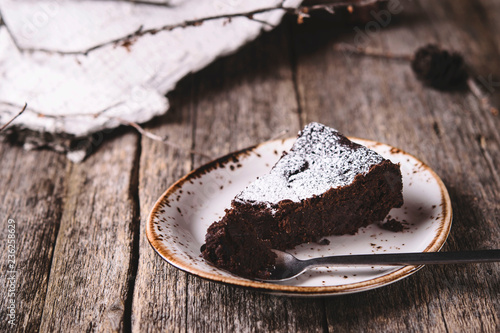 Kladdkaka. Traditional Swedish moist chocolate cake on old rustic wooden table decorated dry twigs, pine cones and birch bark. Fika. Hygge. Toned image photo