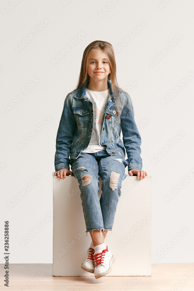 Full length portrait of cute little teen girl in stylish jeans clothes looking at camera and smiling against white studio wall. Kids fashion concept Stock Adobe Stock