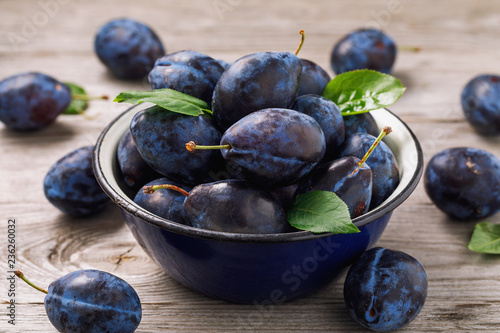 Full bowl of freshly harvested ripe prune fruits on wooden table closeup