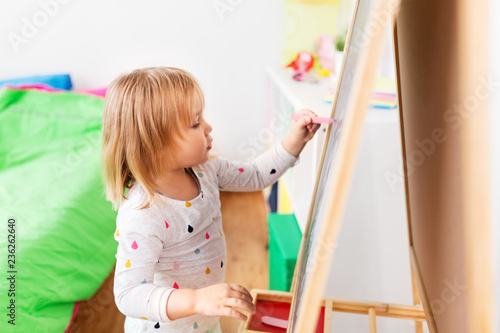 childhood, leisure and people concept - happy little girl drawing on chalk board at home