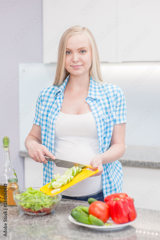 Young pregnant woman at kitchen prepares a vegetable salad Young pregnant woman at kitchen prepares a vegetable salad