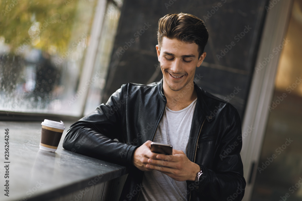© Goran - Smiling young man text messaging on mobile phone