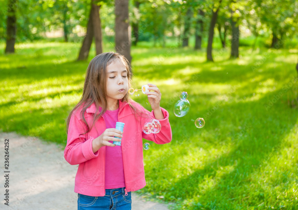 Little girl blowing soap bubbles in summer park. Empty space for text Little girl blowing soap bubbles in summer park. Empty space for text