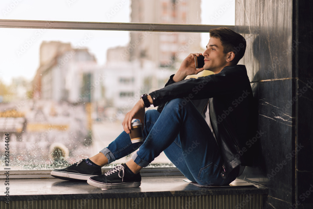 © Goran - Young man talking over cell phone by the window.