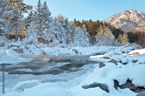 A beautiful winter landscape with a mountain river and a snow-covered trees along the shore on a frosty January afternoon. Eastern Sayan Mountains, Tunka foothill valley, Arshan village