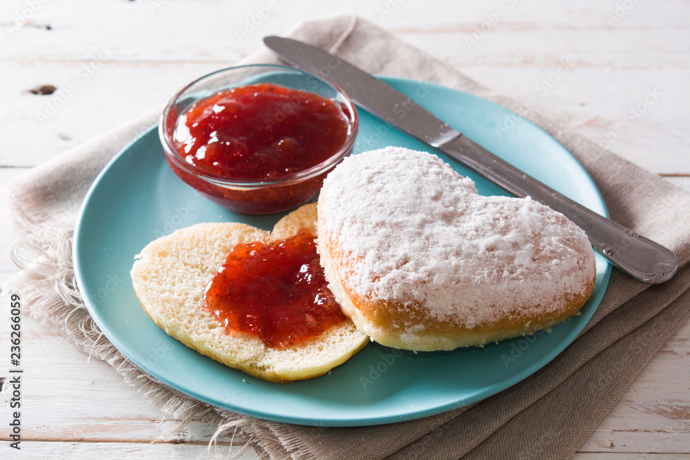 Romantic breakfast with heart-shaped bun and  berry jam on white wooden table. Close up