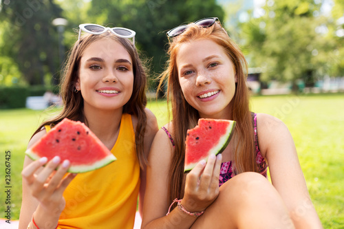 leisure and friendship concept - happy smiling teenage girls or friends eating watermelon at picnic in summer park