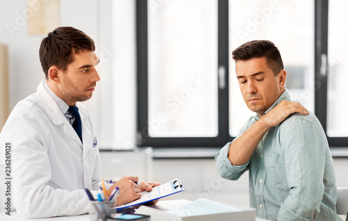 medicine, healthcare and people concept - male patient showing sore arm to doctor at medical office in hospital