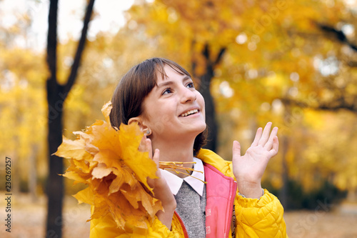 Teen girl is posing with bunch of maple s leaves in autumn park. Beautiful landscape at fall season.
