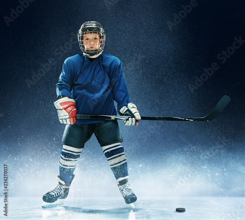 Little boy playing ice hockey at arena. A hockey player in uniform with equipment over a blue background. The athlete, child, sport, action concept photo