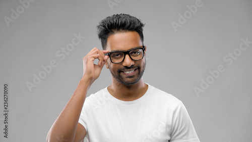 vision, education and people concept - happy smiling indian man in eyeglasses or student over grey background