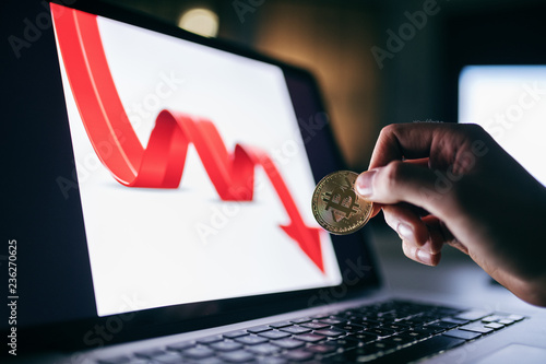 Close up of man holding bit coin. In background arrow on computer pointing down. photo