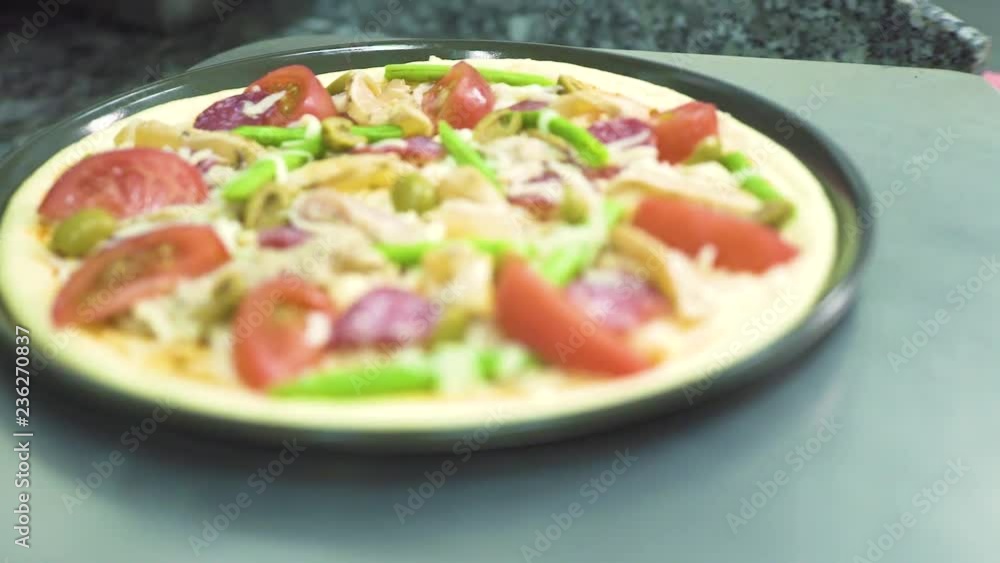 Pizza with pepperoni and tomatoes on kitchen shovel for baking in oven in restaurant. Food cooking concept. Preparing traditional italian pizza in pizzeria kitchen.