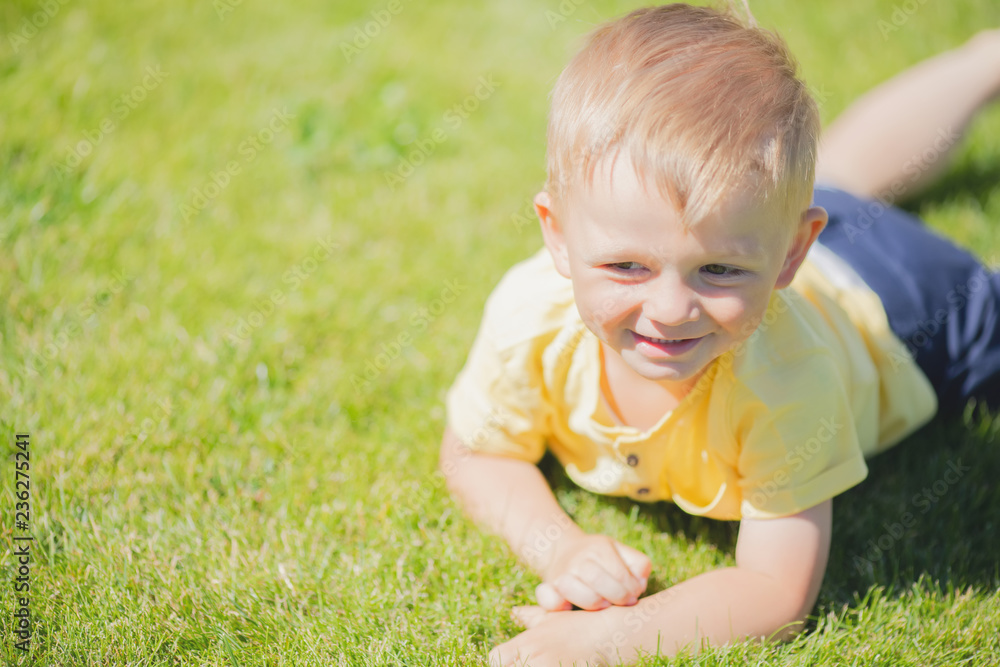 Cute toddler smiling boy lying at the green grass Cute toddler smiling boy lying at the green grass