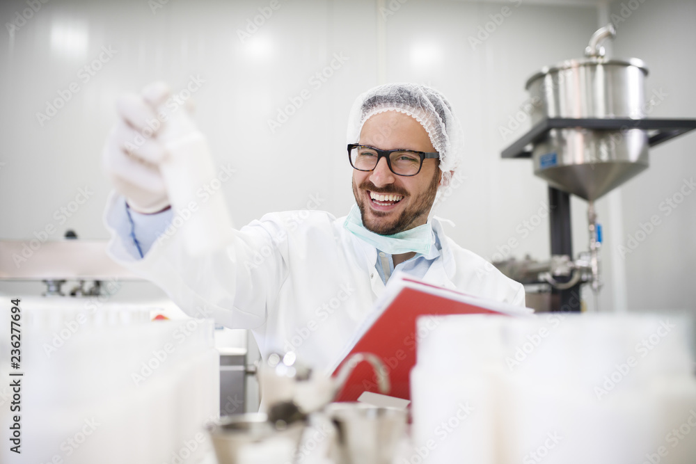 Smiling scientist holding bottle with creme in one hand and test results in other hand while sitting in the lab. Smiling scientist holding bottle with creme in one hand and test results in other hand while sitting in the lab.