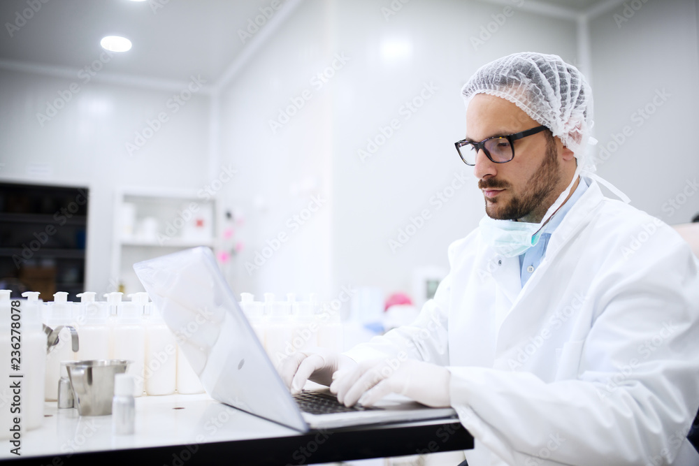Scientist using laptop for entering test results while sitting in the lab. On desk cosmetic products. Scientist using laptop for entering test results while sitting in the lab. On desk cosmetic products.