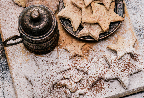 A beautiful Christmas still life of hot black coffee, homemade stars-shaped cookies, cinnamon sticks, flour and sugar sprinkles