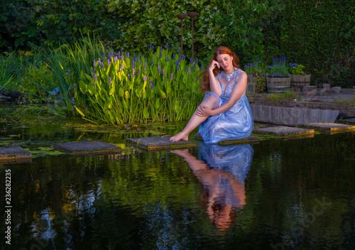 Dreamy model sitting at the edge of a pond in a blue dress. 