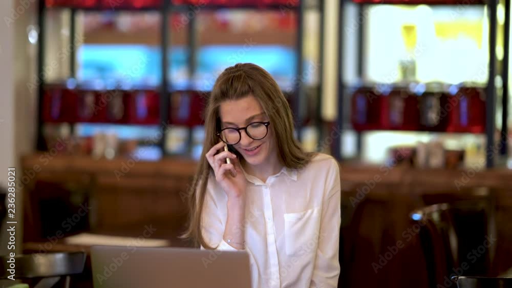A young girl sits in a cafe and talking on the phone, typing on a laptop, drinking tea. Business girl. A young girl sits in a cafe and talking on the phone, typing on a laptop, drinking tea. Business girl.
