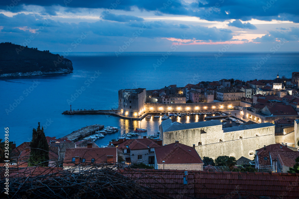 Dubrovnik aerial night view on the harbor after sunset with illuminated fortress wall and dramatic cloudscape, Croatia