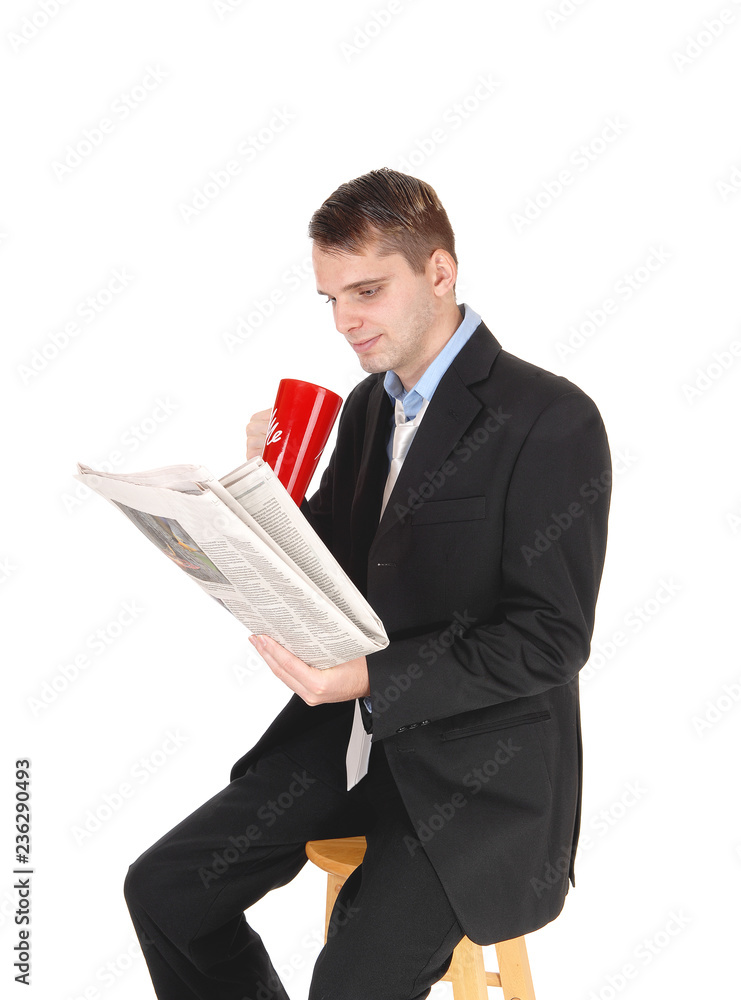 Man sitting in suit drinking and reading paper