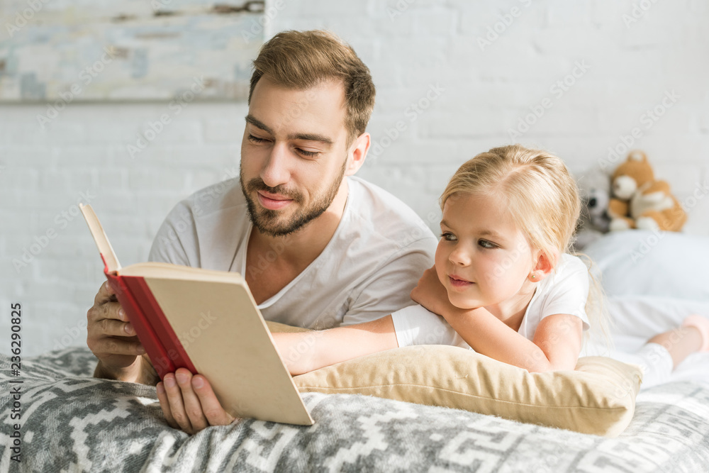 happy father and adorable little daughter lying on bed and reading book happy father and adorable little daughter lying on bed and reading book