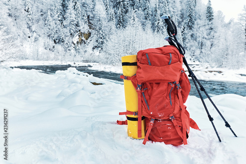 Red backpack with trekkingovymi sticks on the snow in the background of mountains and forests.